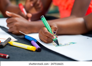 Macro Close Up Of African Kids Hands Drawing With Wax Crayons At Desk.