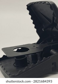 Macro close up of black plastic snap mouse trap. Detailed view of bait pedal with hole, spring mechanism, and serrated grip edges. Reusable rodent trap for pest control isolated on white background.
