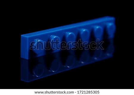 Macro close up of constructor toy blue flat plastic brick isolated on the black reflective background