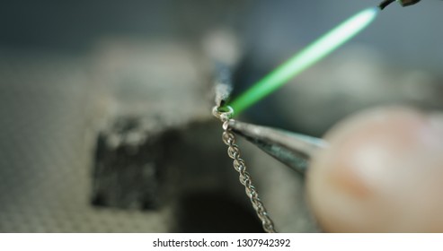 Macro close up of experienced goldsmith working on a handmade jewelry bracelet chain of precious metal white gold in a workshop. Concept of jewelry, luxury, goldsmith, gold, silver, precious metals