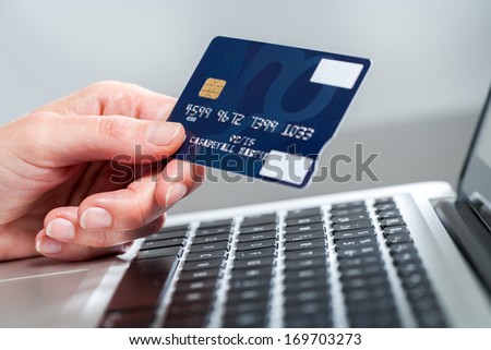 Macro close up of female hand holding credit card on laptop.