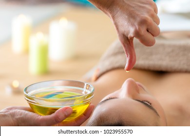 Macro Close Up Of Hand With Oil Drop Above Woman Head In Spa. Aromatic Oil In Glass Bowl Next To Woman At Ayurveda Massage.