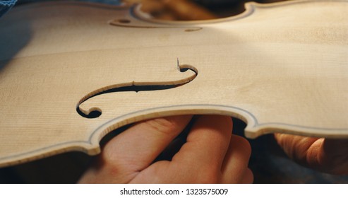 Macro close up of master artisan luthier painstaking detailed work on wood violin in a workshop.