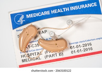 Macro close up of a matched pair of tiny modern hearing aid on medicare card background as coverage is improved