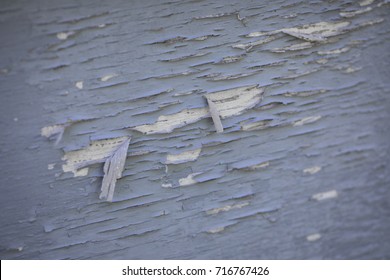 Macro close up on the exterior of an old home with peeling blue paint chips exposed white base primer, presenting a dangerous lead hazard