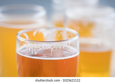 Macro Close Up On The Foam Suds On The Rim Of A Craft Beer Glass, With Assorted Pale Ales In The Blurry Background