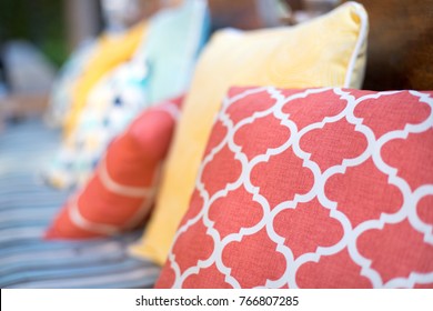 Macro Close Up On Orange And Yellow Pattern Throw Pillows On An Outdoor Patio Chair, With A Blue Striped Cushioned Bench 