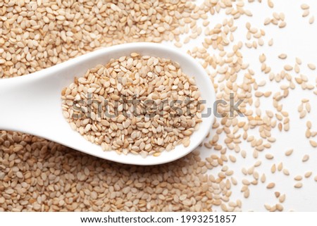Macro Close up of Organic White Sesame seeds(Sesamum indicum) or white Til with shell on a white ceramic soup spoon. Top view,  over gradient background of itself.