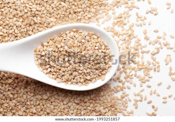 Macro Close up of Organic\
White Sesame seeds(Sesamum indicum) or white Til with shell on a\
white ceramic soup spoon. Top view,  over gradient background of\
itself.