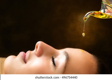 Macro close up portrait of young woman at ayurvedic massage session with aromatic oil dripping on face.