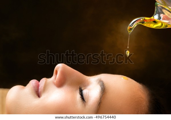 Macro close up portrait of
young woman at ayurvedic massage session with aromatic oil dripping
on face.