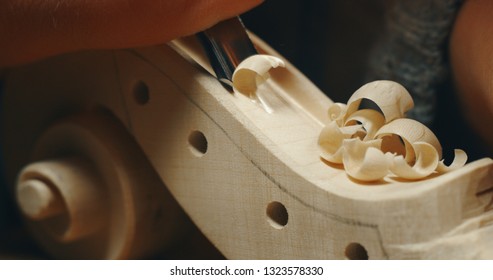 Macro close up of professional master artisan luthier painstaking detailed work on wood violin in a workshop.