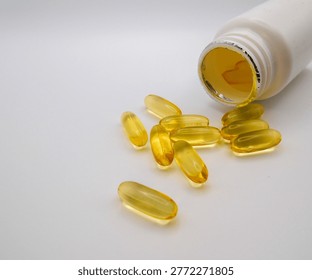 Macro close up view of golden translucent omega 3 fish oil softgel capsules spilling from an open white plastic bottle on clean background highlighting healthcare and nutritional wellness concepts