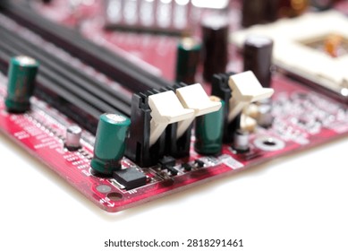 A macro close-up of black DIMM memory slots with white locking clips on a red computer motherboard, surrounded by green capacitors and micro-components.