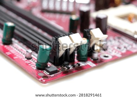A macro close-up of black DIMM memory slots with white locking clips on a red computer motherboard, surrounded by green capacitors and micro-components.