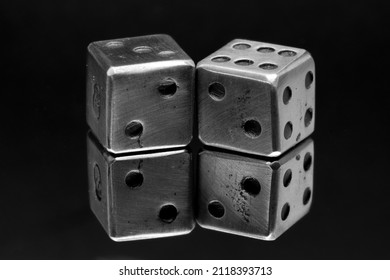 A Macro Closeup Black And White Monochrome Image Of A Pair Of Steel Dice Reflected In A Mirror.  Two Dots Are On The Facing Sides, All Set A Dark Black Background.