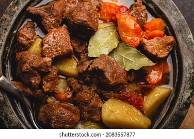 Macro Close-up Of Delicious Beef Meat Stew Dish With Meat Cubes, Potatoes, Carrot And Gravy In Rustic Metal Bowl On Brown Concrete Background Top View