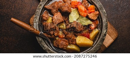 Macro close-up of delicious beef meat stew dish with meat cubes, potatoes, carrot and gravy in rustic metal bowl on brown concrete background top view