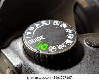 Macro close-up of a DSLR camera mode dial showing auto and guide settings in bright lighting