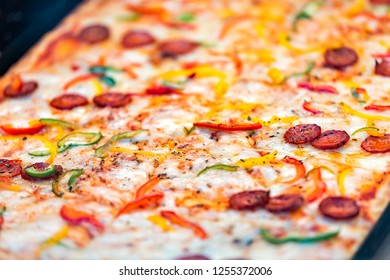 Macro Closeup Of Fresh Thin Crust Rectangular Pizza In Store Cafe On Display Restaurant In Italy With Melted Shiny Mozzarella Cheese, Pepperoni Meat Slices, Red Bell Shredded Peppers