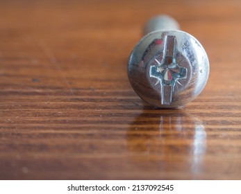 Macro Close-up Of A Galvanized Steel Screw Head On A Wooden Table With Reflection. Screw On A Wooden Background, Working Tools. Screw Cap Close-up On A Wooden Surface.