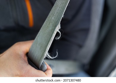 Macro closeup of man driver or passenger holding pulling old frayed ripped torn damaged car vehicle seat belt or seatbelt