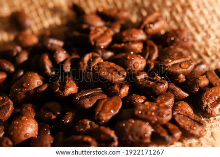 Macro closeup of pile fresh roasted organic wet coffee beans with water drops on jute fabric sack (focus on center)