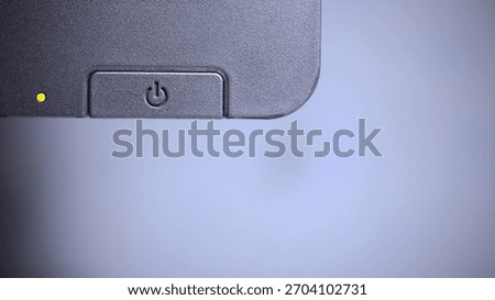 Macro close-up of a power button with indicator light on the corner of a computer monitor, with clean copy space, representing on off control, start up, shutdown, and modern electronic technology.