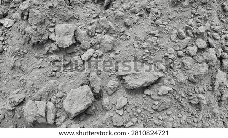 . A macro close-up of rough, clumpy soil mixed with small rocks and gravel, highlighting the uneven, raw texture of a dry, uncultivated natural ground surface.
