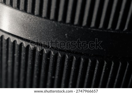 Macro closeup selective focus of a ridged black camera lens barrel's extreme detail, showcasing fine texture with a pleasing bokeh blur for microstock.