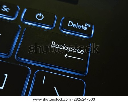 Macro close-up shot of the Backspace key and power button on a modern black backlit laptop keyboard glowing in the dark.