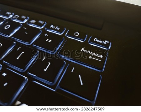 Macro close-up shot of the Backspace key and power button on a modern black backlit laptop keyboard glowing in the dark.