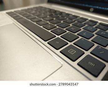 A macro, close-up shot captures the keyboard and trackpad of a silver laptop from a side angle. The black chiclet keys are in sharp focus around the spacebar, 