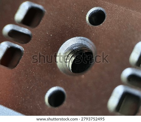 A macro close-up shot showcasing the threaded central screw hole mount interface on a brown anodized metal base plate, surrounded by geometric rectangular weight-reduction cutouts.
