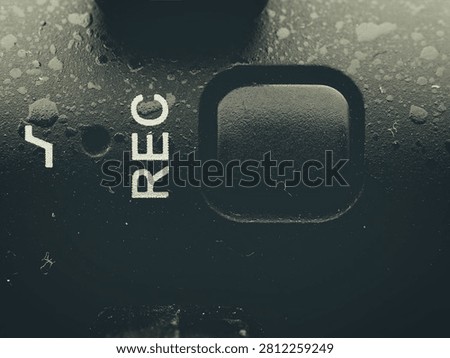 Macro closeup of a square black record button with printed white REC text on a dirty textured electronic device body panel
