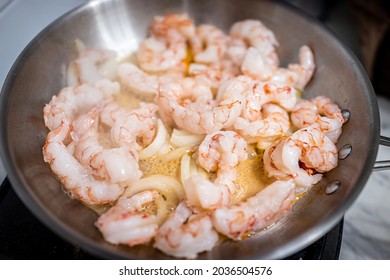 Macro Closeup Of Stainless Steel Frying Pan With Sauteing Olive Oil, Sweet Onion Slices And Whole Large King Jumbo Argentinian Shrimp Seafood Cooked On Electric Stove In Home Kitchen