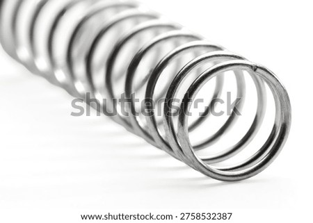 Macro close-up of a steel compression spring lying on its side, showing the circular coil cross-section with bokeh background. Metallic texture and industrial detail.