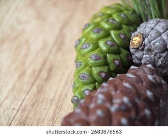 Macro close-up of three pine cones on light brown wooden background, one green cone and two closed brown cones, natural woodland seeds, rustic forest detail, organic botanical macro photo