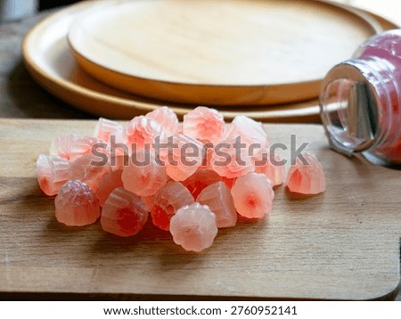 Macro close-up of translucent pink red flower-shaped health gummy vitamin supplement candy piled on wooden surface with warm bokeh