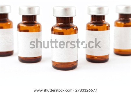 Macro close-up view of a row of amber glass medical vials with blank labels on white background. Selective focus and shallow depth of field representing pharmaceutical research, precision in medicine, or vaccine quality control.