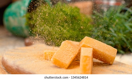 MACRO, DOF: Aromatic Parmesan Flakes Fall Down On The Cheese Cubes Served On A Wooden Board. Mouth-watering Shot Of Yellow Parmesan Cheese Being Grated Over The Whole Cheese Cubes. Italian Delicacy.
