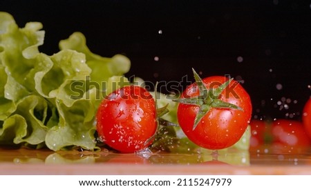 MACRO, DOF: Cleaned salad ingredients land on the kitchen counter. Cinematic shot of wet tomatoes falling and rolling around a wooden countertop. Organic lettuce and ripe tomatoes on cutting board.