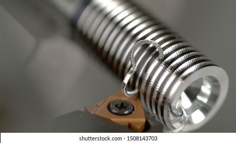 MACRO, DOF: CNC Machine Slowly Threading A Small Metal Workpiece Into A Shiny Screw. Sharp Metal Cutter Carving Deep Grooves Into A Shiny Silver Colored Workpiece During Thread Cutting Process.