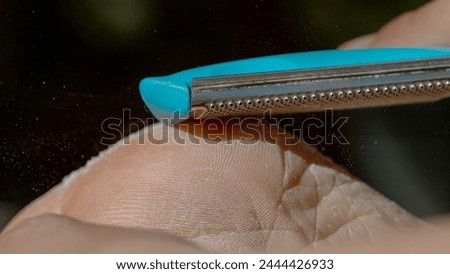 MACRO, DOF: Detailed closeup of showing the removal of dry skin with a specialized pedicure file. Macro shot of a foot being exfoliated with blue pedicure tool, capturing flurry of skin particles.
