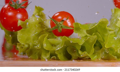 MACRO, DOF: Detailed View Of Ripe Cherry Tomatoes Falling Onto The Wet Chopping Board. Bright Red Tomatoes Fall And Land Onto The Romaine Lettuce Leaves Sitting On The Chef's Cluttered Cutting Board.