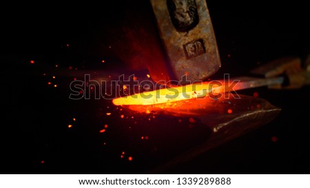 MACRO, DOF: Red hot piece of metal is being held by iron tongs and struck by a big hammer. Glowing particles flying away from a knife blade being manufactured by experienced bladesmith. Sparks flying.