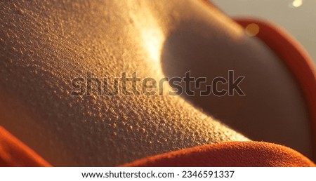 MACRO, DOF: Shivering female skin with goosebumps in beautiful golden sunlight. Young woman on a walk at sunset, chilled by a cold summer breeze. She is underdressed for a summer evening at seaside.