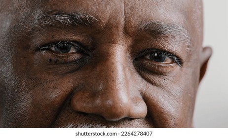 Macro extreme close up half part of face elderly middle-aged African old wrinkled man with dark eyes sad calm mature male senior citizen looking at camera myopia vision sight problem poor eyesight - Powered by Shutterstock