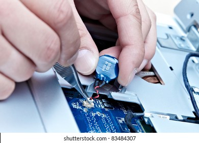 macro of hands with tweezers disconnecting a laptop battery