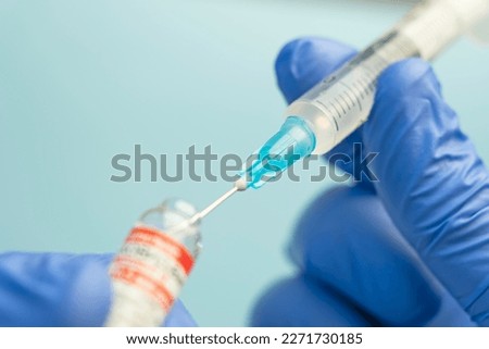 Macro of a hypodermic syringe or needle being filled with mRNA vaccine from bottle against a blue background